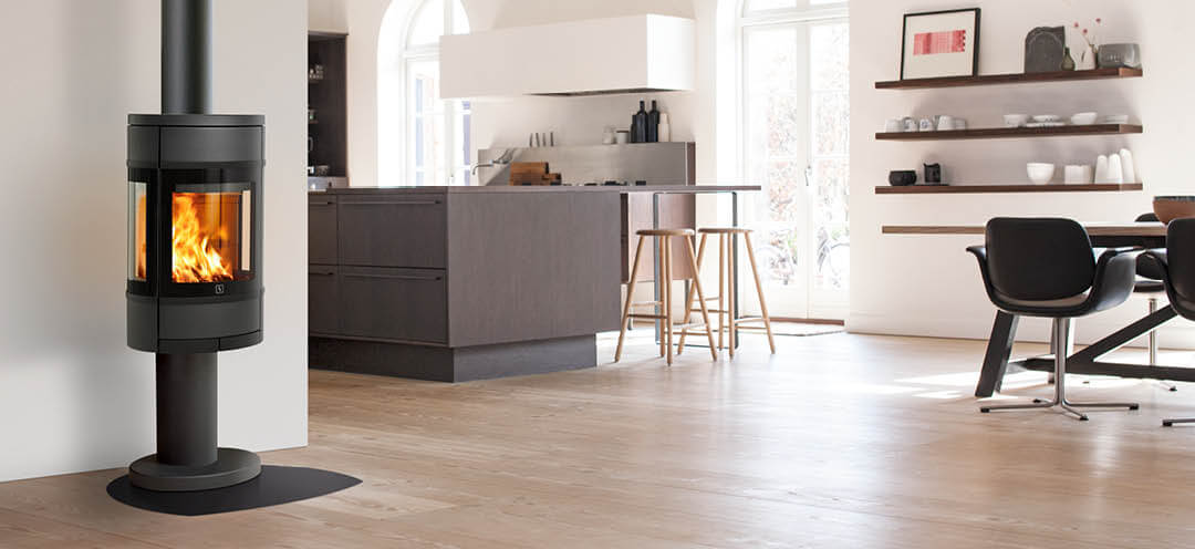 Oval, svart braskamin med sidoglas Scan 68-9 på pelare placerad i ljust kök med modern brun inredning