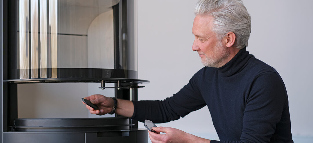 Medelålders man i höghalsad tröja designern Niels Kjeldsen visar glashandtag framför eldstaden Scan 87