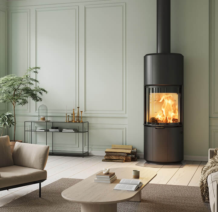 Stor svart öppen spis Scan 87 I ljusgrönt rum med ljusa designmöbler, ett svart konsolbord och stor planta i hörnet