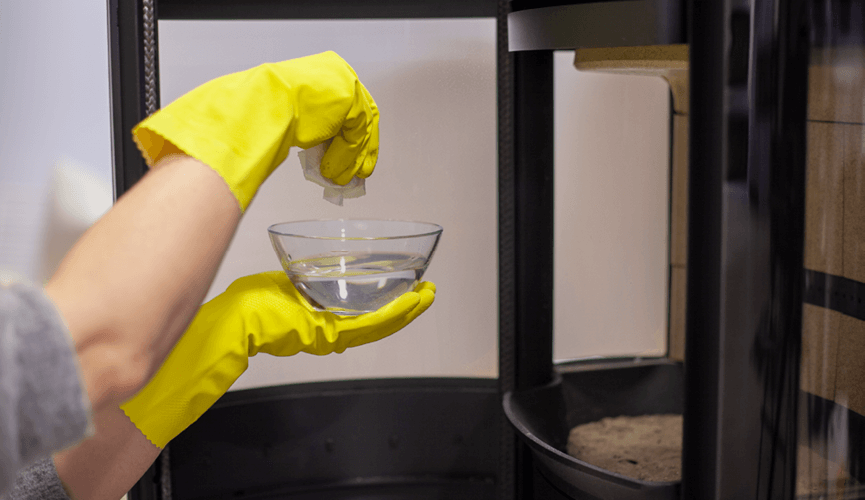 Hand med gul handske dopppapper i en skål med vatten