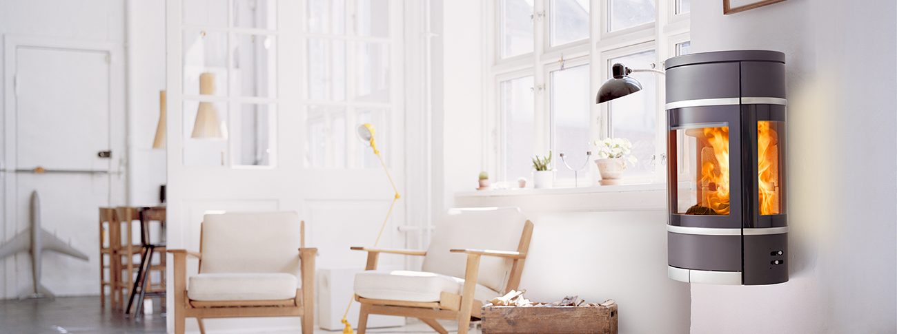 Svart oval vägghängd braskamin med sidohandtag av aluminium och dekorlister Scan 68-8 i ett vitt rum med ljusa möbler i dansk designstil