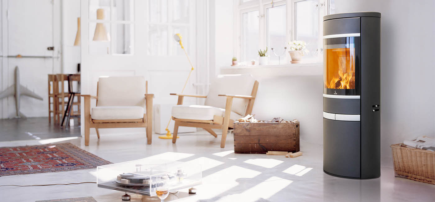 Svart oval braskamin Scan 68-13 i ett modernt vardagsrum med ljusa möbler och stora fönster mot ett snölandskap