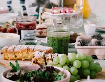 Påskdekorerat bord med rosa skålar och buffé med bröd, vindruvor, pesto och mycket mer