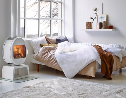 Vit braskamin Scan 66 i vit ettrumsstuga bredvid säng och skrivbord i ved