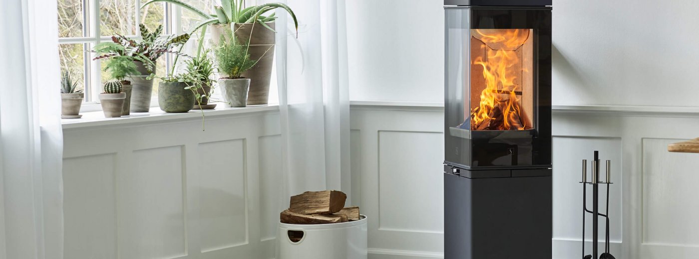 Den höga svarta öppen spis är nära den vita väggen och fönstret.