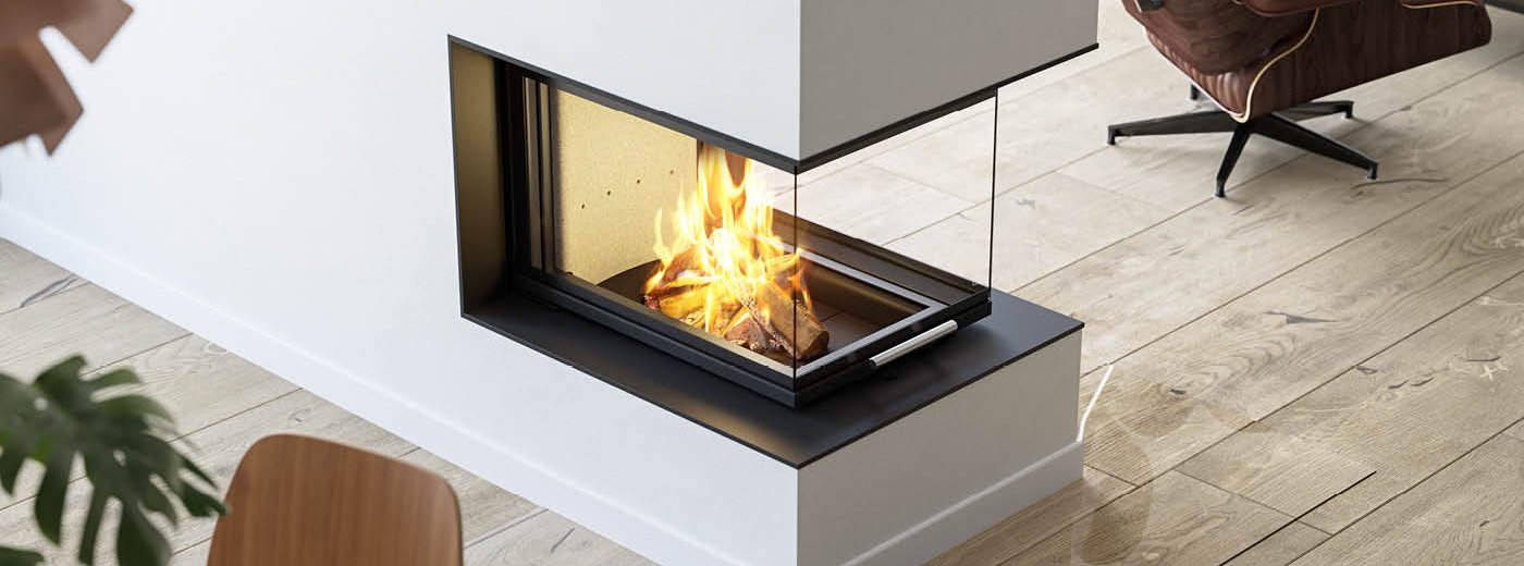 Bilde tatt ovenfra av stor peisinnsats Scan 5005 FRL med glass på tre sider og hevedør på rustikt tregulv og brun skinnstol ved siden